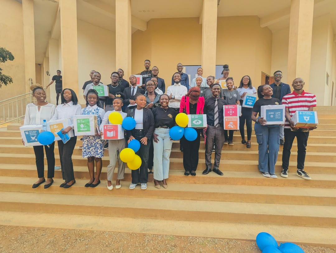 Young people celebrating with Sustainable Development Goals boxes on the steps of a community hall